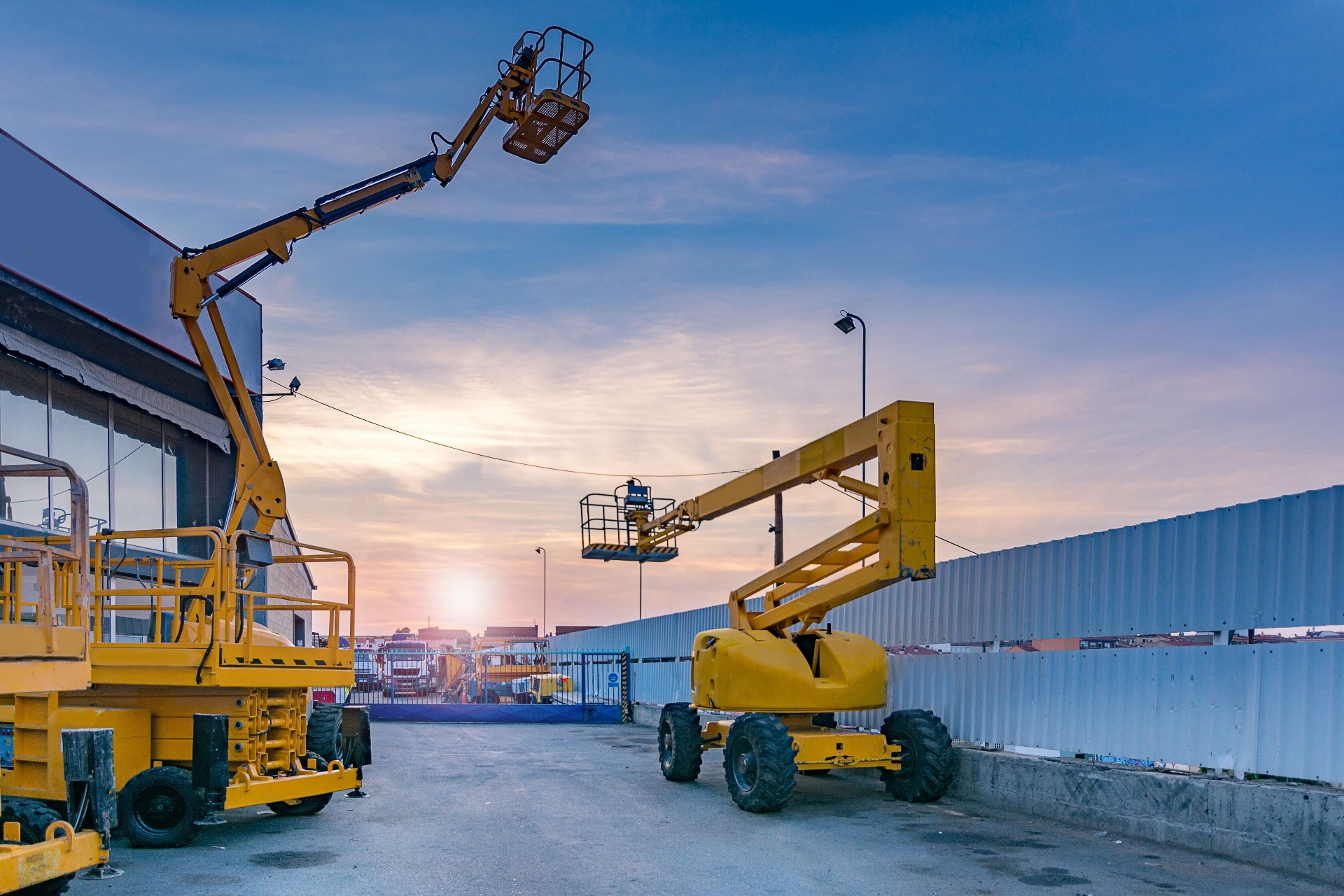 Yellow articulated boom lift and scissor lift at a yard during golden hour