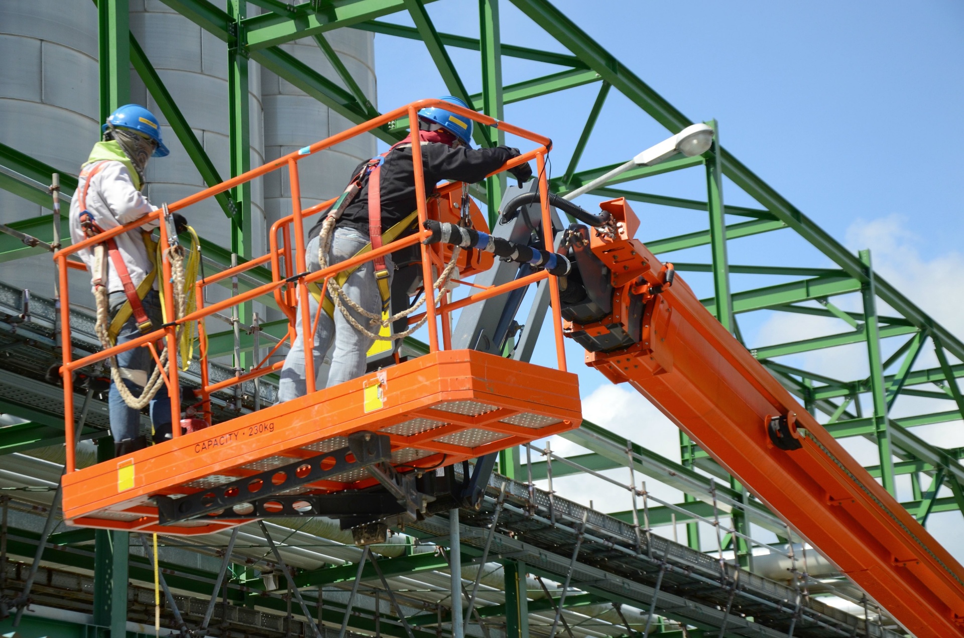 Two harnessed workers operating an aerial boom lift platform on a job site