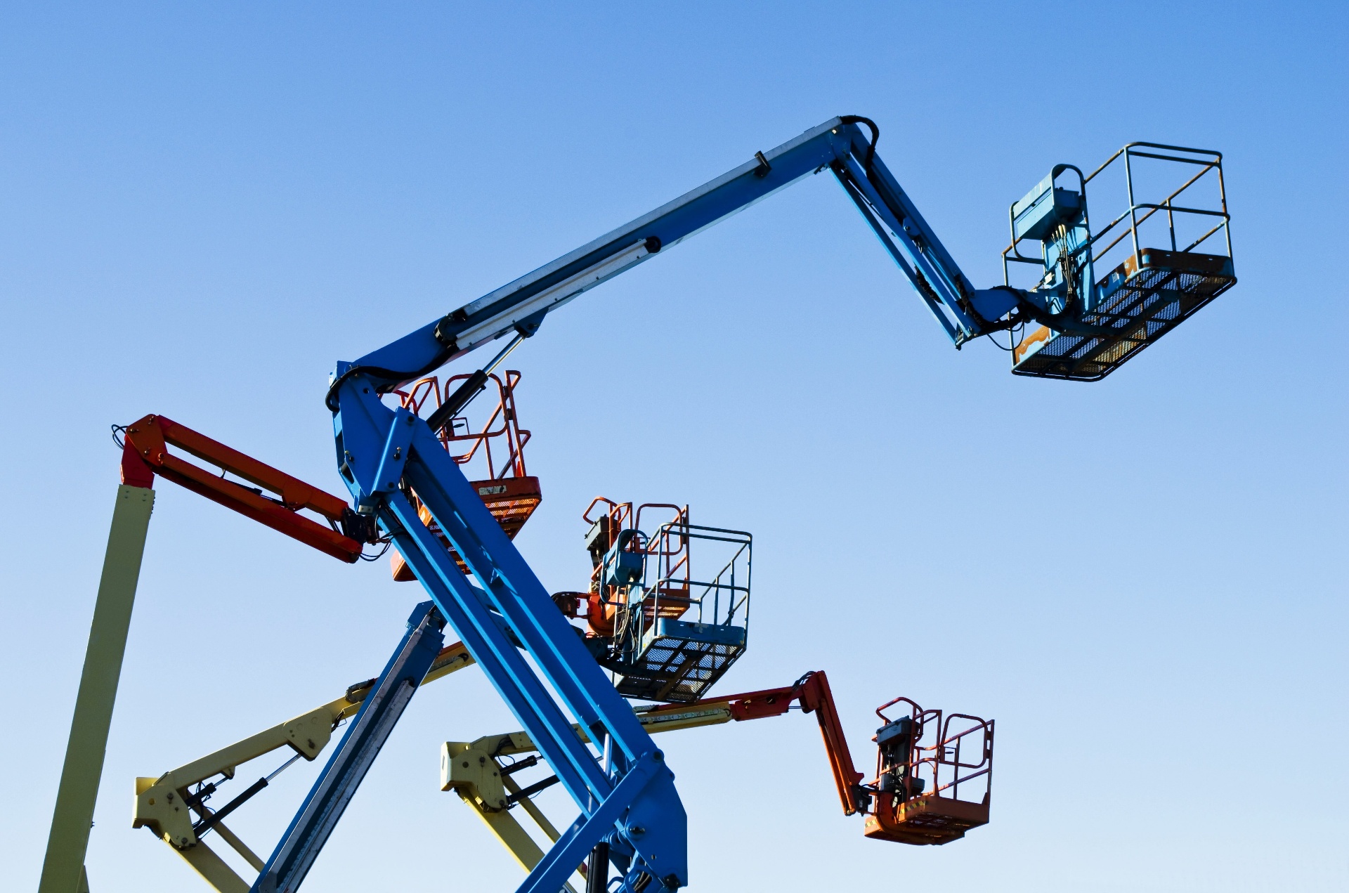 Articulated boom lifts and scissor lifts staged against blue sky