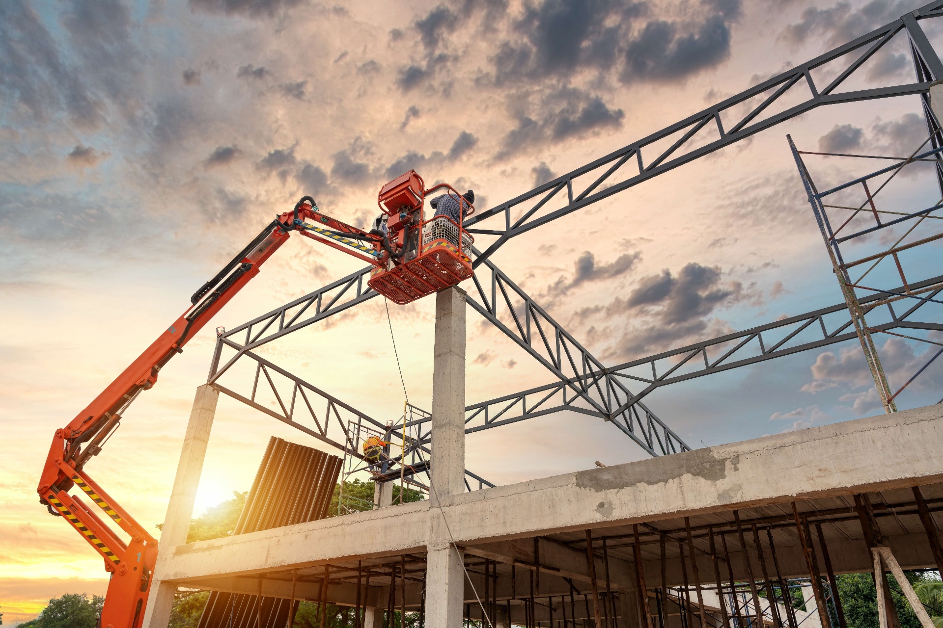 Operator on aerial boom lift platform at sunset above a steel structure