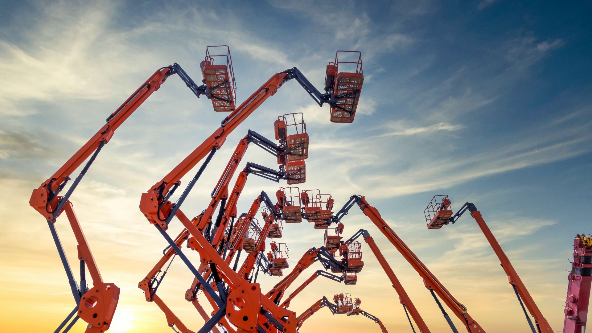 Fleet of aerial work platforms silhouetted against sunset sky